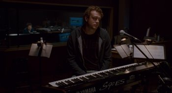 Movie still from “Forgetting Sarah Marshall” (2008), directed by Nicholas Stoller – A man sitting in front of a keyboard in front of a microphone; Medium shot, Over the shoulder angle
