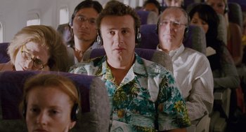 Movie still from “Forgetting Sarah Marshall” (2008), directed by Nicholas Stoller – A man in a hawaiian shirt is on a plane with other passengers; Medium shot, Over the shoulder angle