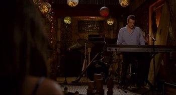 Movie still from “Forgetting Sarah Marshall” (2008), directed by Nicholas Stoller – A man playing a keyboard in front of a group of people; Wide shot, Over the shoulder angle