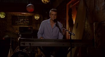 Movie still from “Forgetting Sarah Marshall” (2008), directed by Nicholas Stoller – A man standing at a keyboard in front of a microphone; Medium shot, Over the shoulder angle