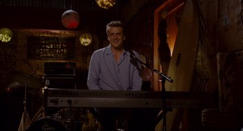 Movie still from “Forgetting Sarah Marshall” (2008), directed by Nicholas Stoller – A man standing at a keyboard in front of a microphone; Medium shot, Over the shoulder angle
