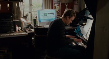 Movie still from “Forgetting Sarah Marshall” (2008), directed by Nicholas Stoller – A man sitting in front of a computer keyboard; Medium shot, Over the shoulder angle
