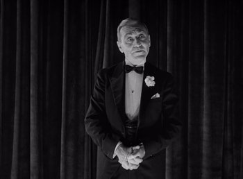 Movie still from “Frankenstein” (1931), directed by James Whale – An older man in a tuxedo standing in front of a curtain; Medium shot, Low angle