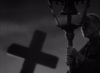 Movie still from “Frankenstein” (1931), directed by James Whale – A person holding a cross behind a bell; Medium shot, Low angle