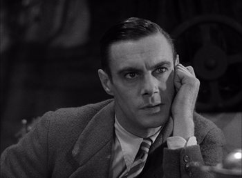 Movie still from “Frankenstein” (1931), directed by James Whale – A man in a suit and tie holding his hand up to his ear; Close Up shot, Low angle