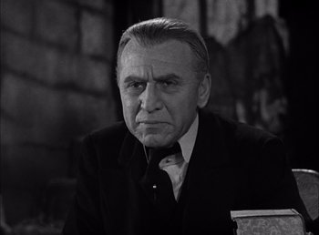 Movie still from “Frankenstein” (1931), directed by James Whale – An older man in a black suit and white shirt; Close Up shot, Low angle