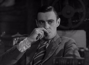 Movie still from “Frankenstein” (1931), directed by James Whale – A man wearing a suit and tie sitting in front of a clock; Close Up shot, Low angle