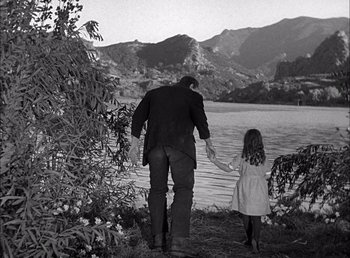 Movie still from “Frankenstein” (1931), directed by James Whale – A man and a little girl holding hands near a body of water; Wide shot, Over the shoulder angle