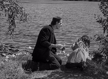 Movie still from “Frankenstein” (1931), directed by James Whale – A man kneeling down next to a little girl near a body of water; Wide shot, Over the shoulder angle