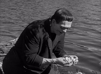 Movie still from “Frankenstein” (1931), directed by James Whale – A man in a black jacket holding a flower in a body of water; Medium shot, Low angle