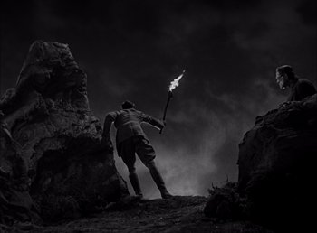 Movie still from “Frankenstein” (1931), directed by James Whale – A man holding a stick with a flame on it; Wide shot, Low angle