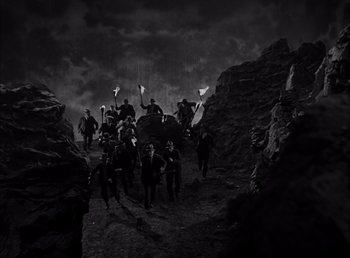 Movie still from “Frankenstein” (1931), directed by James Whale – A black and white photo of a group of people walking through a rocky area; Wide shot, High angle