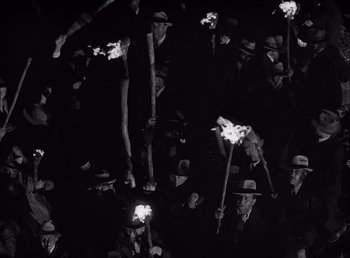 Movie still from “Frankenstein” (1931), directed by James Whale – A group of men holding lit torches in the dark; Wide shot, High angle