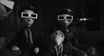 Movie still from “Frankenweenie” (2012), directed by Tim Burton – A black and white photo of a couple and a dog wearing 3 d glasses; Medium shot, Over the shoulder angle