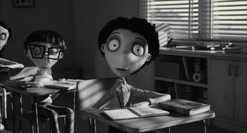 Movie still from “Frankenweenie” (2012), directed by Tim Burton – A black - and - white photo of a person sitting at a desk; Medium shot, Over the shoulder angle