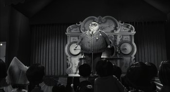 Movie still from “Frankenweenie” (2012), directed by Tim Burton – A man standing in front of a microphone on a stage; Wide shot, Low angle