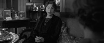 Movie still from “Frantz” (2016), directed by François Ozon – An older woman sitting on a couch in a living room; Medium shot, Over the shoulder angle