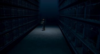 Movie still from “Free Birds” (2013), directed by Jimmy Hayward – A man standing in a dark room in front of shelves of books; Extreme Wide shot, High angle