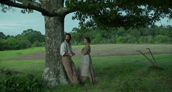 Movie still from “Free State of Jones” (2016), directed by Gary Ross – A man and a woman standing next to a tree in a field; Wide shot, High angle