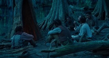 Movie still from “Free State of Jones” (2016), directed by Gary Ross – A group of people sitting in the woods at night; Wide shot, Over the shoulder angle