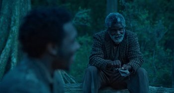 Movie still from “Free State of Jones” (2016), directed by Gary Ross – A man sitting on top of a wooden bench next to another man; Medium shot, Over the shoulder angle