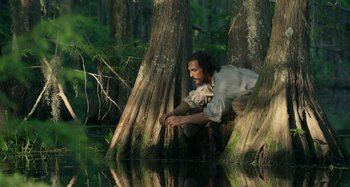 Movie still from “Free State of Jones” (2016), directed by Gary Ross – A man sitting on a tree in the middle of a swamp; Wide shot, High angle