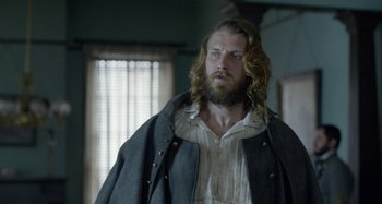 Movie still from “Free State of Jones” (2016), directed by Gary Ross – A man with long hair and a beard wearing a jacket; Medium shot, Over the shoulder angle