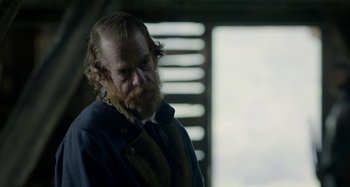 Movie still from “Free State of Jones” (2016), directed by Gary Ross – A man with long hair and a beard is standing in front of a window; Medium shot, Over the shoulder angle