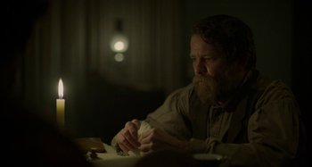Movie still from “Free State of Jones” (2016), directed by Gary Ross – A man sitting at a dinner table with food in front of him; Medium shot, Over the shoulder angle