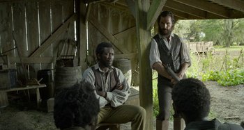 Movie still from “Free State of Jones” (2016), directed by Gary Ross – Two men in old time clothing sitting in a barn; Medium shot, Over the shoulder angle
