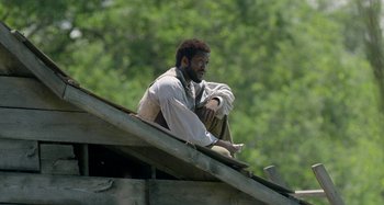 Movie still from “Free State of Jones” (2016), directed by Gary Ross – A man sitting on top of a wooden structure; Medium shot, Low angle