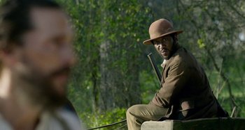 Movie still from “Free State of Jones” (2016), directed by Gary Ross – A man sitting on top of a bench holding a rifle; Medium shot, Over the shoulder angle