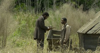 Movie still from “Free State of Jones” (2016), directed by Gary Ross – Two men standing in a field looking at a piece of paper; Wide shot, Over the shoulder angle