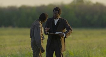 Movie still from “Free State of Jones” (2016), directed by Gary Ross – Two men standing in the grass talking to each other; Medium shot, Over the shoulder angle