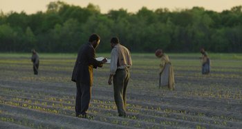 Movie still from “Free State of Jones” (2016), directed by Gary Ross – Two men are in a field and one of them is holding a frisbee; Wide shot, Over the shoulder angle