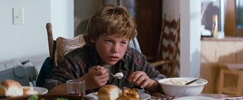 Movie still from “Free Willy” (1993), directed by Simon Wincer – A young boy sitting at a table eating a sandwich; Close Up shot, High angle