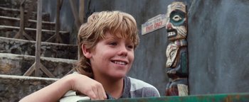Movie still from “Free Willy” (1993), directed by Simon Wincer – A young boy smiling for the camera in front of an exit sign; Close Up shot, Low angle