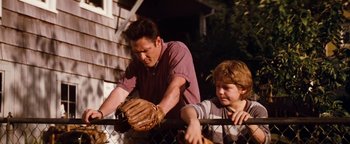 Movie still from “Free Willy” (1993), directed by Simon Wincer – A man and a boy with a baseball glove on a fence; Medium shot, Low angle
