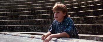Movie still from “Free Willy” (1993), directed by Simon Wincer – A young boy sitting on a ledge next to steps; Close Up shot, Low angle