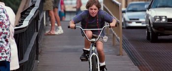 Movie still from “Free Willy” (1993), directed by Simon Wincer – A young boy riding a bike down a sidewalk; Medium shot, Low angle