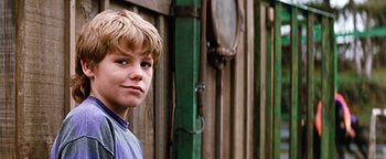 Movie still from “Free Willy” (1993), directed by Simon Wincer – A young boy standing in front of a wooden fence; Close Up shot, Low angle
