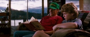 Movie still from “Free Willy” (1993), directed by Simon Wincer – A man sitting on a couch while reading a book; Medium shot, Over the shoulder angle