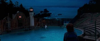 Movie still from “Free Willy” (1993), directed by Simon Wincer – A man standing next to a swimming pool at night; Extreme Wide shot, High angle