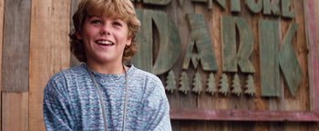 Movie still from “Free Willy” (1993), directed by Simon Wincer – A young man smiling in front of a wooden sign; Close Up shot, Low angle