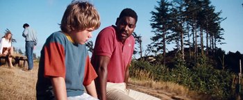 Movie still from “Free Willy” (1993), directed by Simon Wincer – Two young men sitting on the ground in front of a forest; Medium shot, Low angle