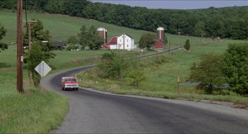 Movie still from “Friday the 13th” (1980), directed by Sean S. Cunningham – A car driving down a road near a farm; Extreme Wide shot, High angle