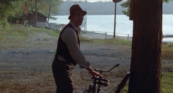 Movie still from “Friday the 13th” (1980), directed by Sean S. Cunningham – An older man standing next to a bicycle near a lake; Wide shot, Over the shoulder angle