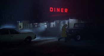 Movie still from “Friday the 13th” (1980), directed by Sean S. Cunningham – A man walking in the rain in front of a diner at night; Extreme Wide shot, High angle