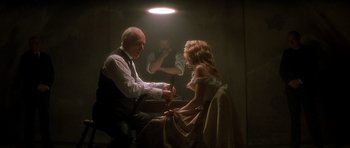 Movie still from “From Hell” (2001), directed by Allen Hughes – A man and a woman sitting in front of a man holding a knife; Medium shot, Low angle