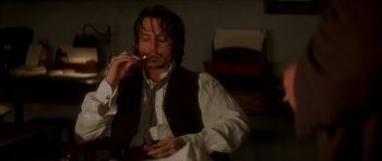 Movie still from “From Hell” (2001), directed by Allen Hughes – A man smoking a cigarette while sitting down; Medium shot, Low angle